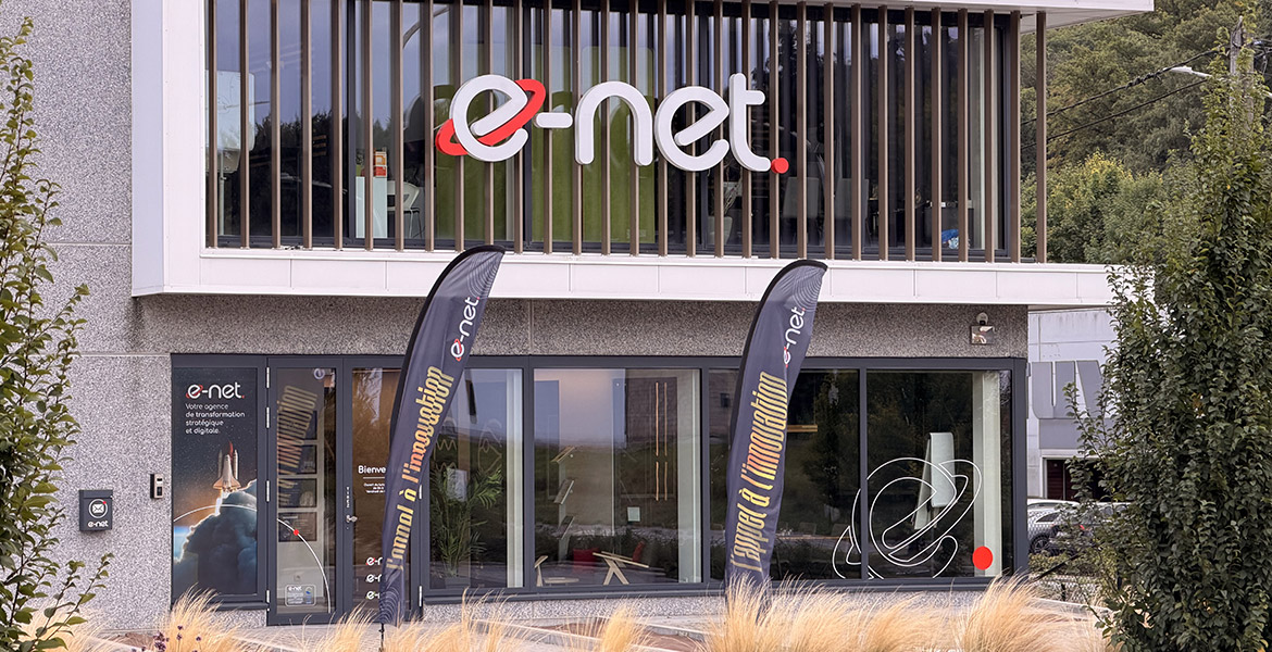 Façade du bâtiment e-net. avec son logo et des bannières 'Appel à l’innovation' devant l’entrée.