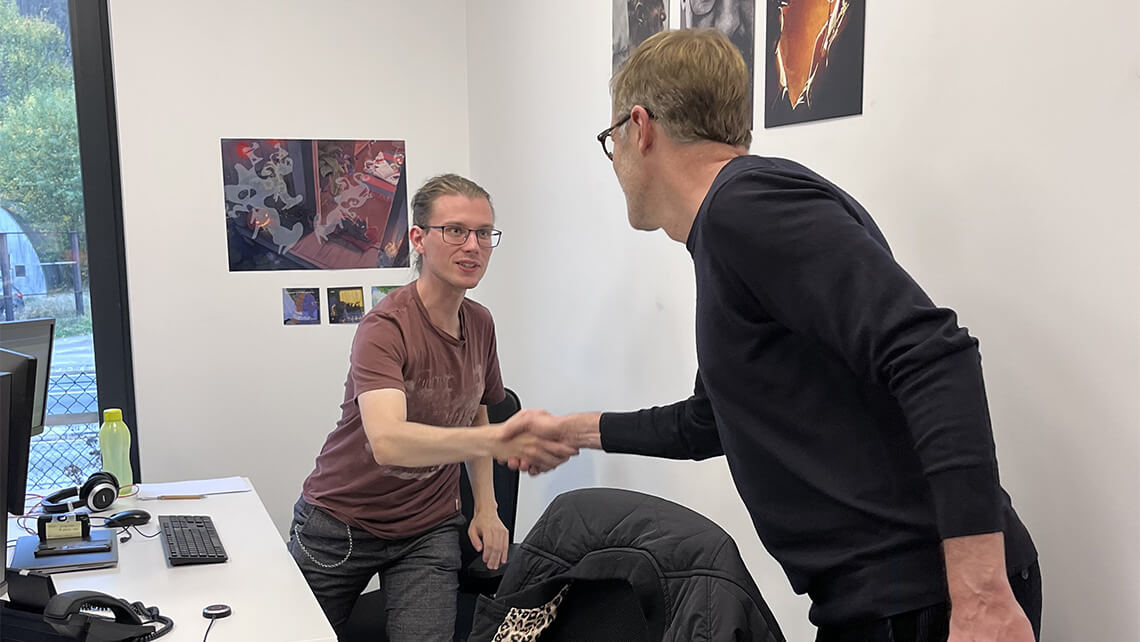 Paul Magnette et Valentin, concepteur - diffuseur chez e-net. group, échangent une poignée de main dynamique lors de la visite des bureaux e-net. group.  