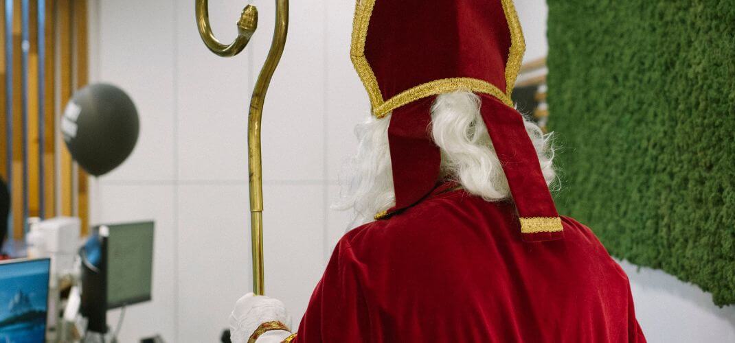 Saint-Nicolas dans les locaux e-net, vue de dos avec manteau rouge, mitre et crosse dorée.