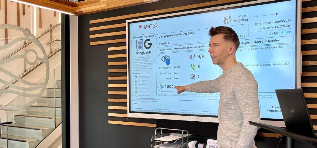 Présentation dans les locaux e-net, avec Sacha Peiffer pointant des résultats affichés sur un grand écran lors d’un rapport Google Ads
