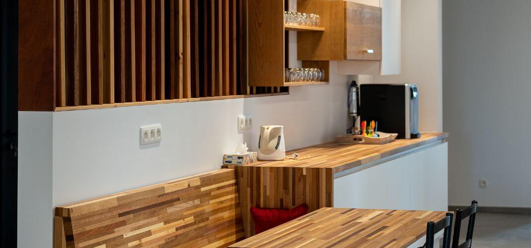 Coin cuisine des locaux e-net avec plan de travail en bois, étagères ouvertes, machine à café, bouilloire et table en bois avec banc assorti.